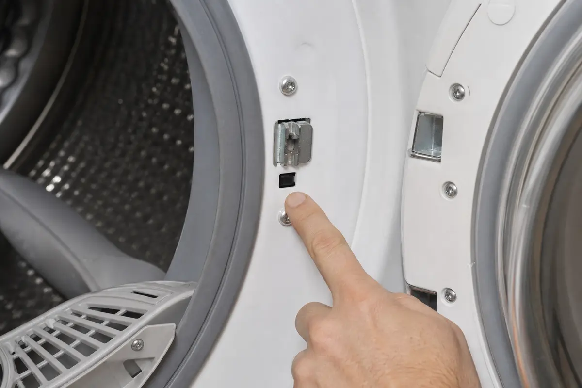 Open LG-style dryer door frame with latch and door switch area being inspected