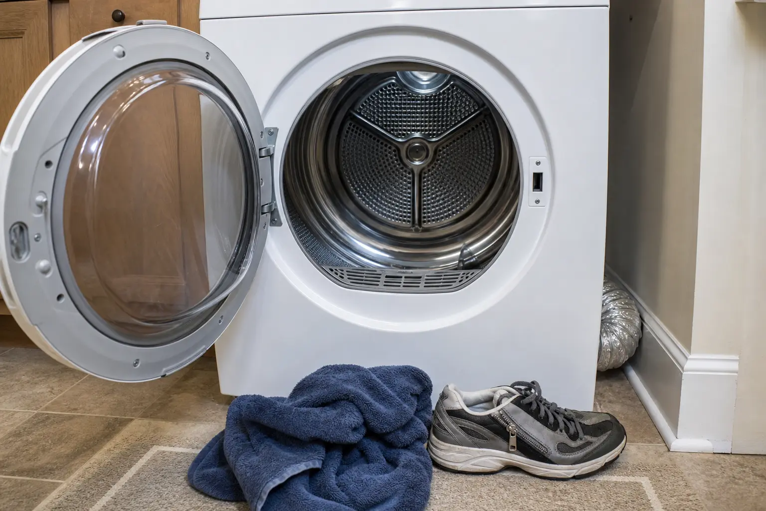 Open LG-style dryer with empty drum, towel, and shoe used to separate load thump from machine thump