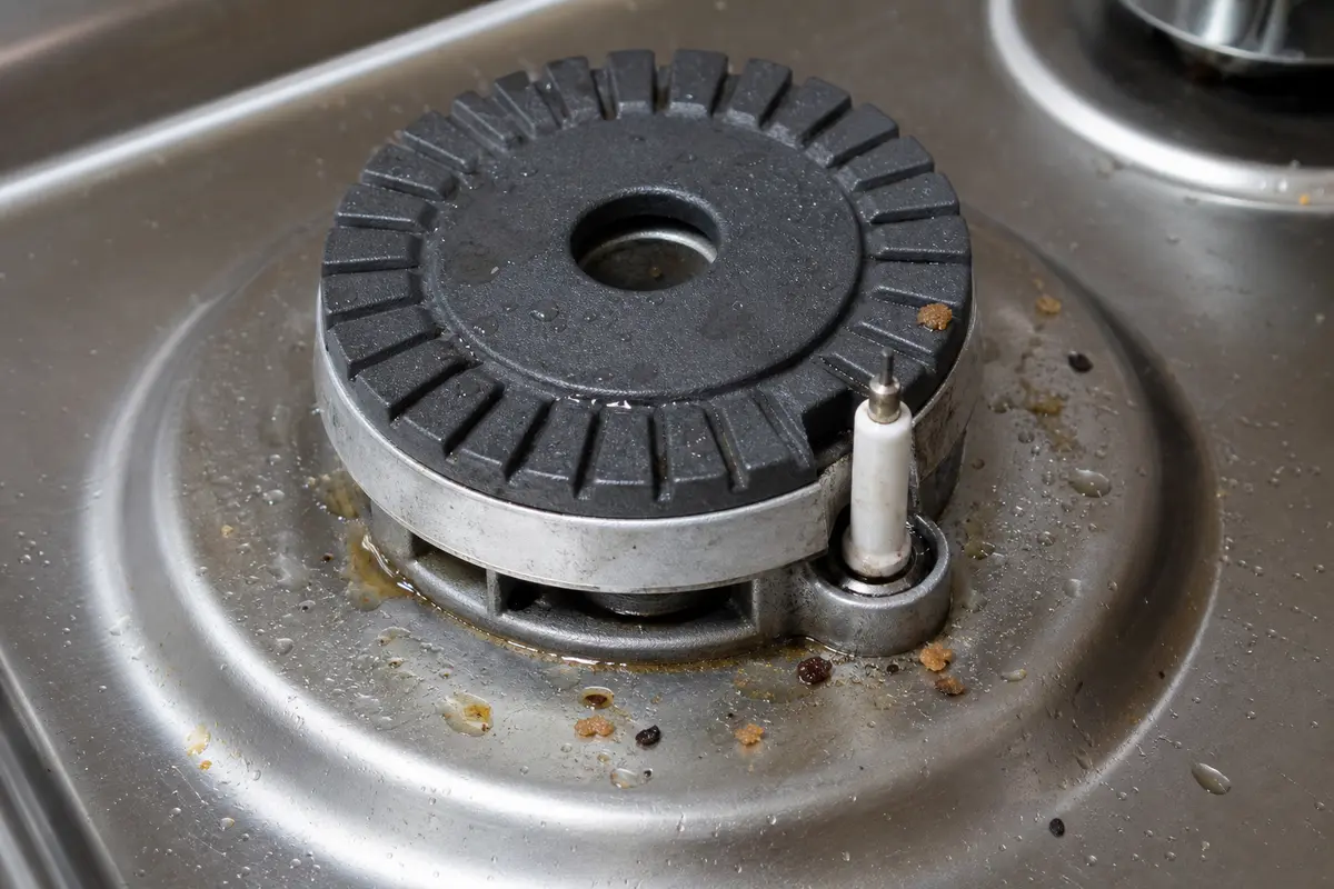 LG cooktop burner igniter close-up with moisture and food debris near the spark point