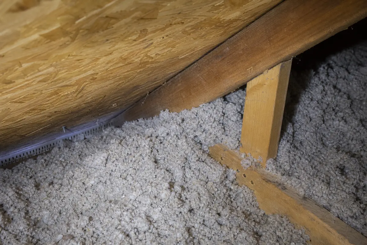 Loose attic insulation piled at the roof edge where a soffit air channel should stay open