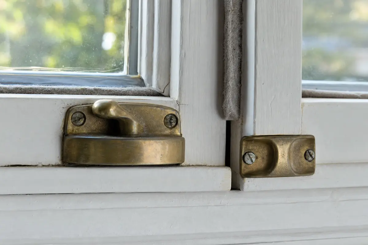 Close view of a window latch keeper and worn weatherstripping gap that can cause wind rattle