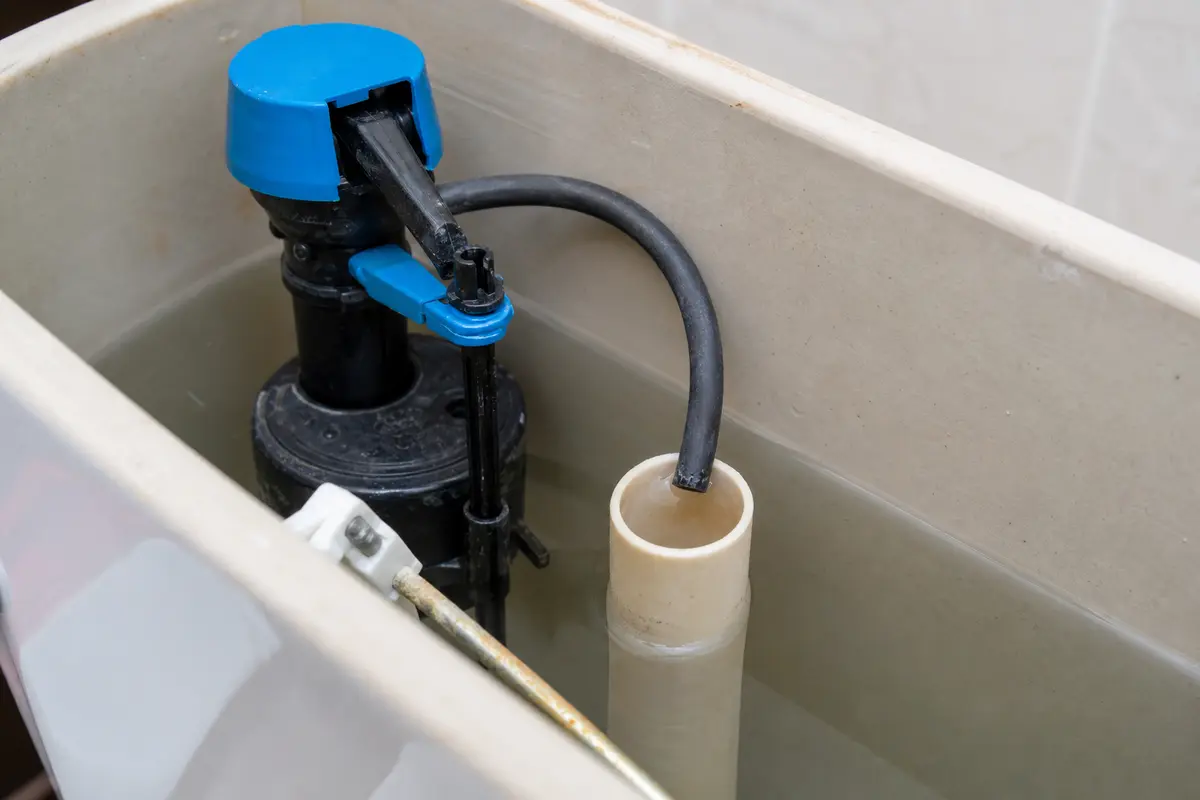 Toilet tank with fill valve float and overflow tube visible for adjustment
