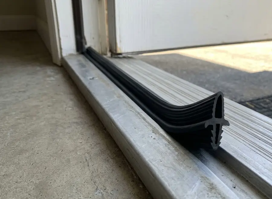 Close-up of a black exterior door threshold seal partly seated in an aluminum threshold channel