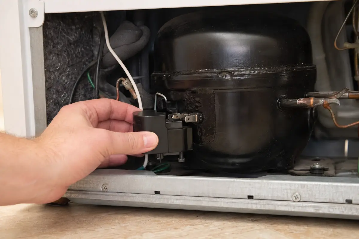 Hand lining up freezer start relay on compressor pins