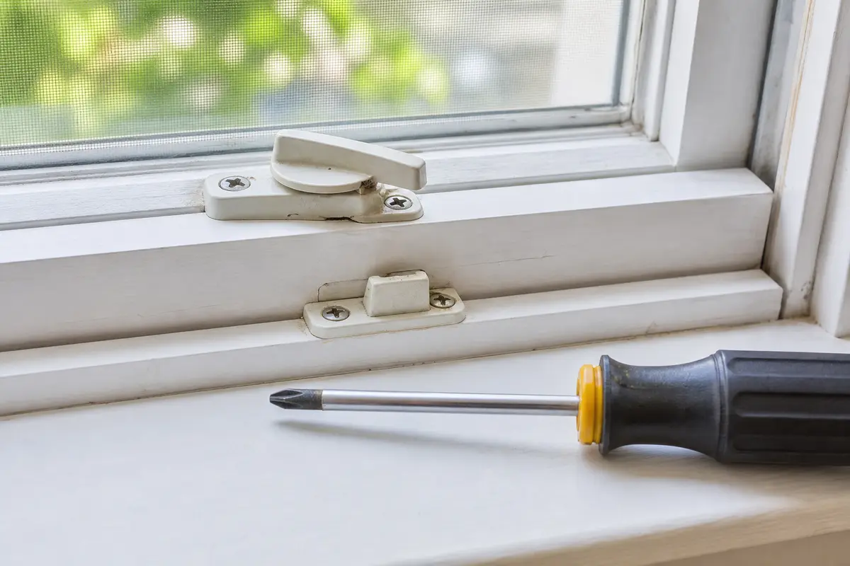 Phillips screwdriver staged beside a window latch for tightening loose keeper screws